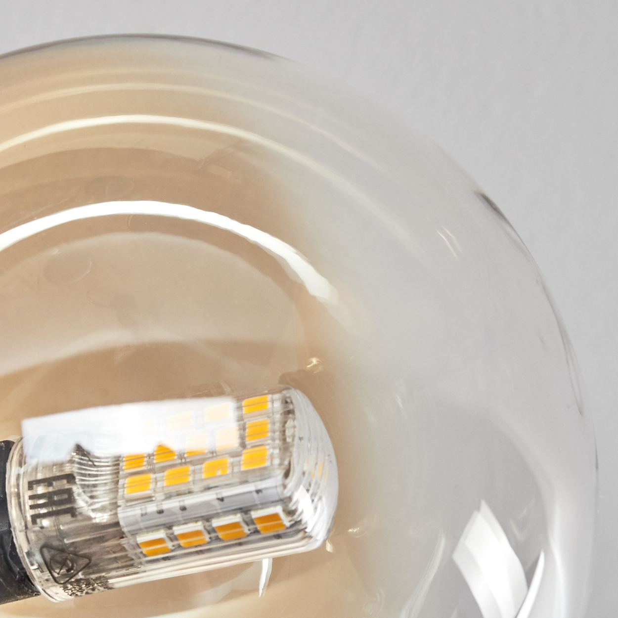 Nahaufnahme einer Glühbirne. Die Birne ist transparent mit warmem Glanz. Der Sockel der Birne ist schwarz mit einer kleinen, rechteckigen Lichtquelle.