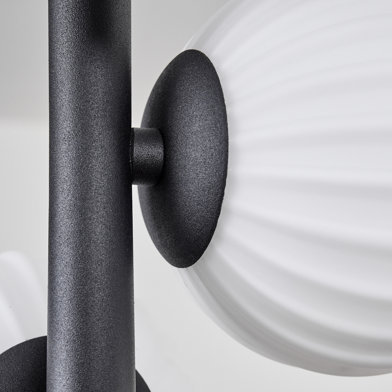 Nahaufnahme einer modernen Lampe. Sie hat schwarze Metallstützen und weiße, gerippte Glaskugeln. Der Hintergrund ist weiß.