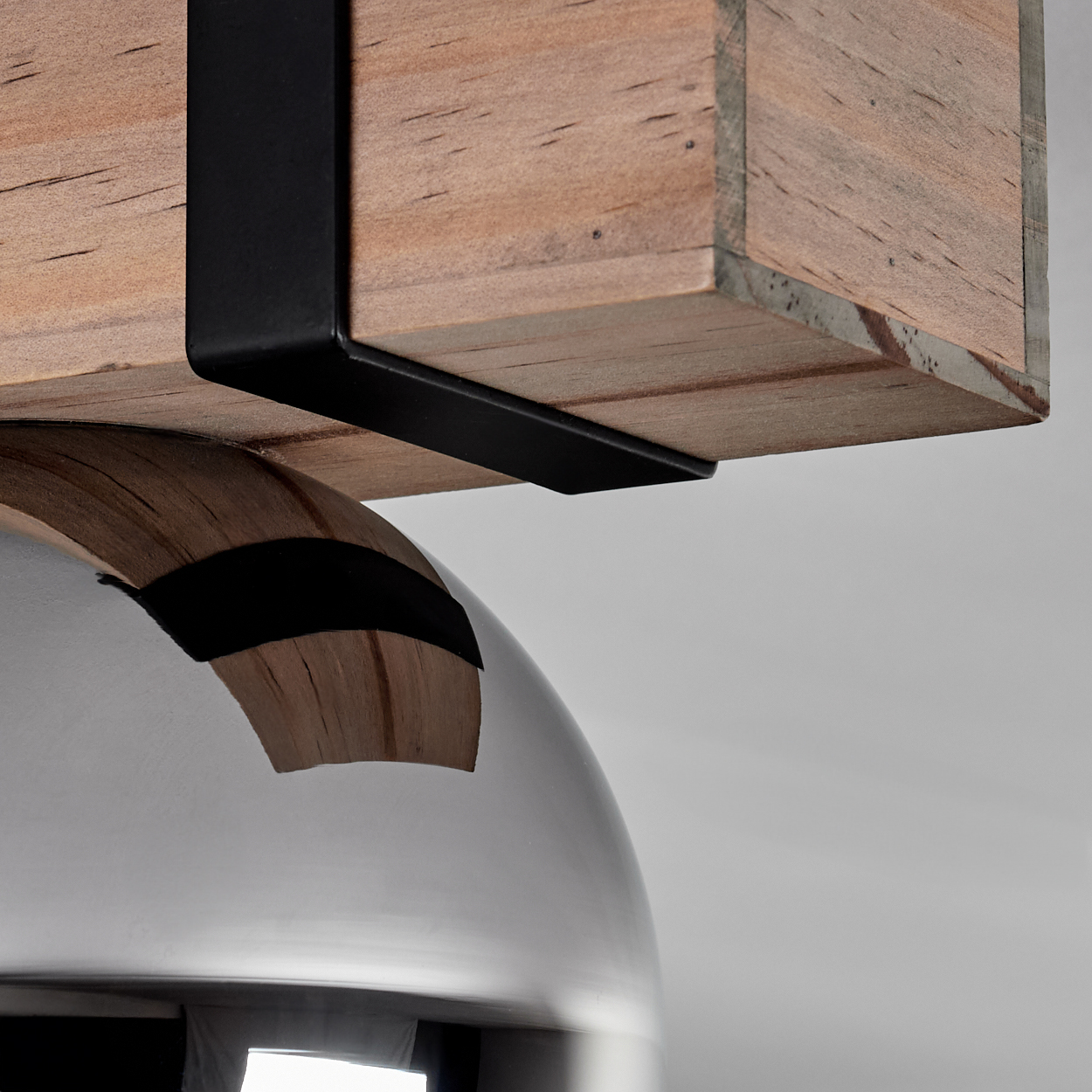 Nahaufnahme eines Holzbalkens, der von schwarzen Metallbügeln gehalten wird, über einer gebogenen, metallischen Oberfläche. Der Hintergrund ist schlicht weiß.