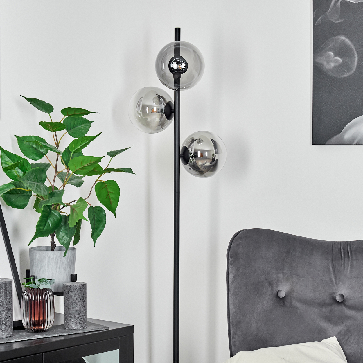 Ein modernes Wohnzimmer mit einer schwarzen Lampe mit Glaskugeln, einer grünen Pflanze und einem grauen Kopfteil.