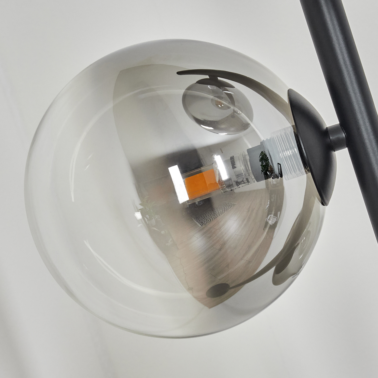 Nahaufnahme einer modernen Lampe mit einer großen, klaren Glaskugel, die das Innere eines Raumes widerspiegelt. Schwarzes Metall stützt die Kugel.