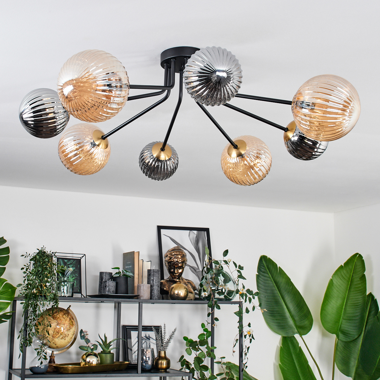 Eine moderne Deckenlampe mit mehreren runden Glaskugeln in Gold- und Silberfarben. Darunter ein Regal mit Pflanzen und Dekoration.