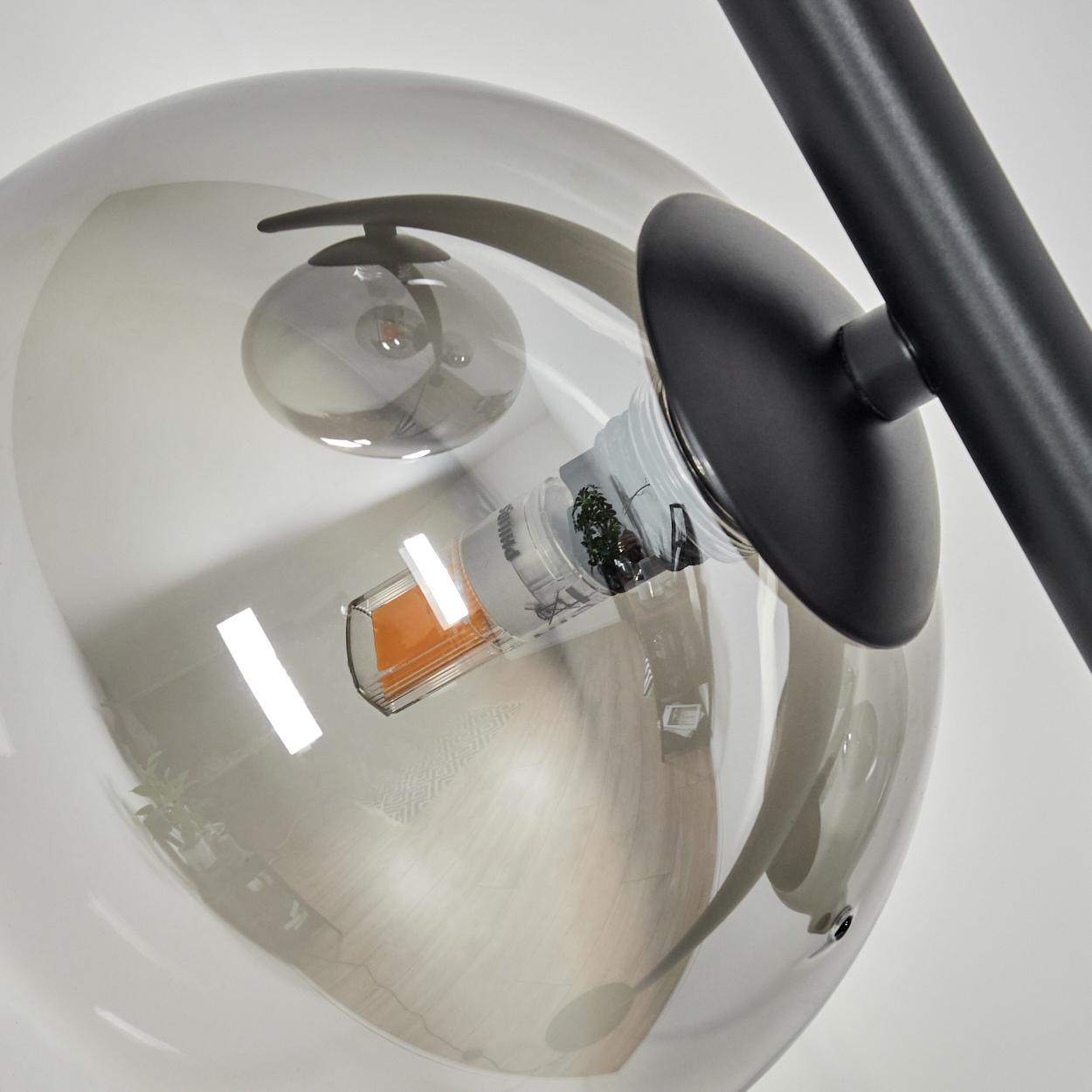 Nahaufnahme einer modernen Lampe. Ein klarer Glaskolben umschließt eine Glühbirne. Schwarzes Metall stützt den Globus. Der Hintergrund ist weiß.