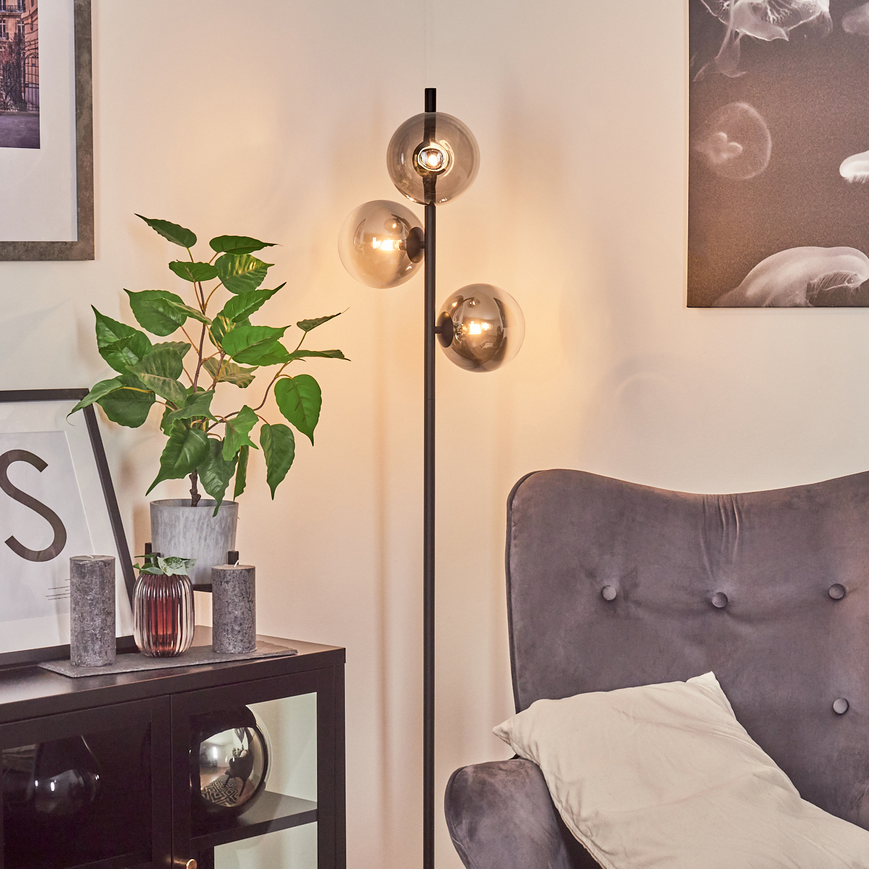 Ein modernes Wohnzimmer mit Stehlampe, grauem Sessel und schwarzem Schrank mit Dekorationsartikeln.