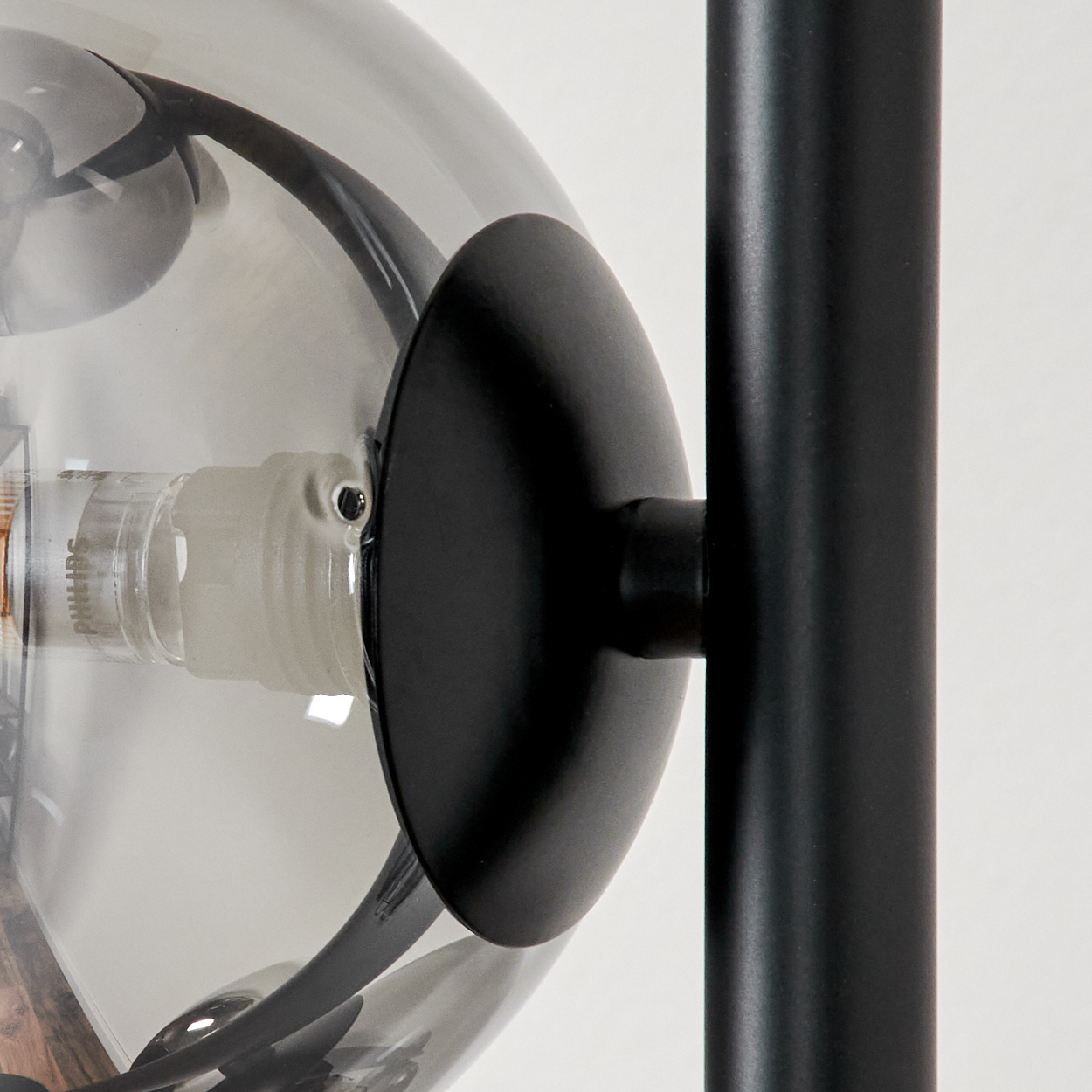 Nahaufnahme einer modernen Lampe. Ein schwarzer Metallpfosten und ein runder, rauchiger Glasschirm. Ein schwarzes rundes Teil befestigt den Schirm.