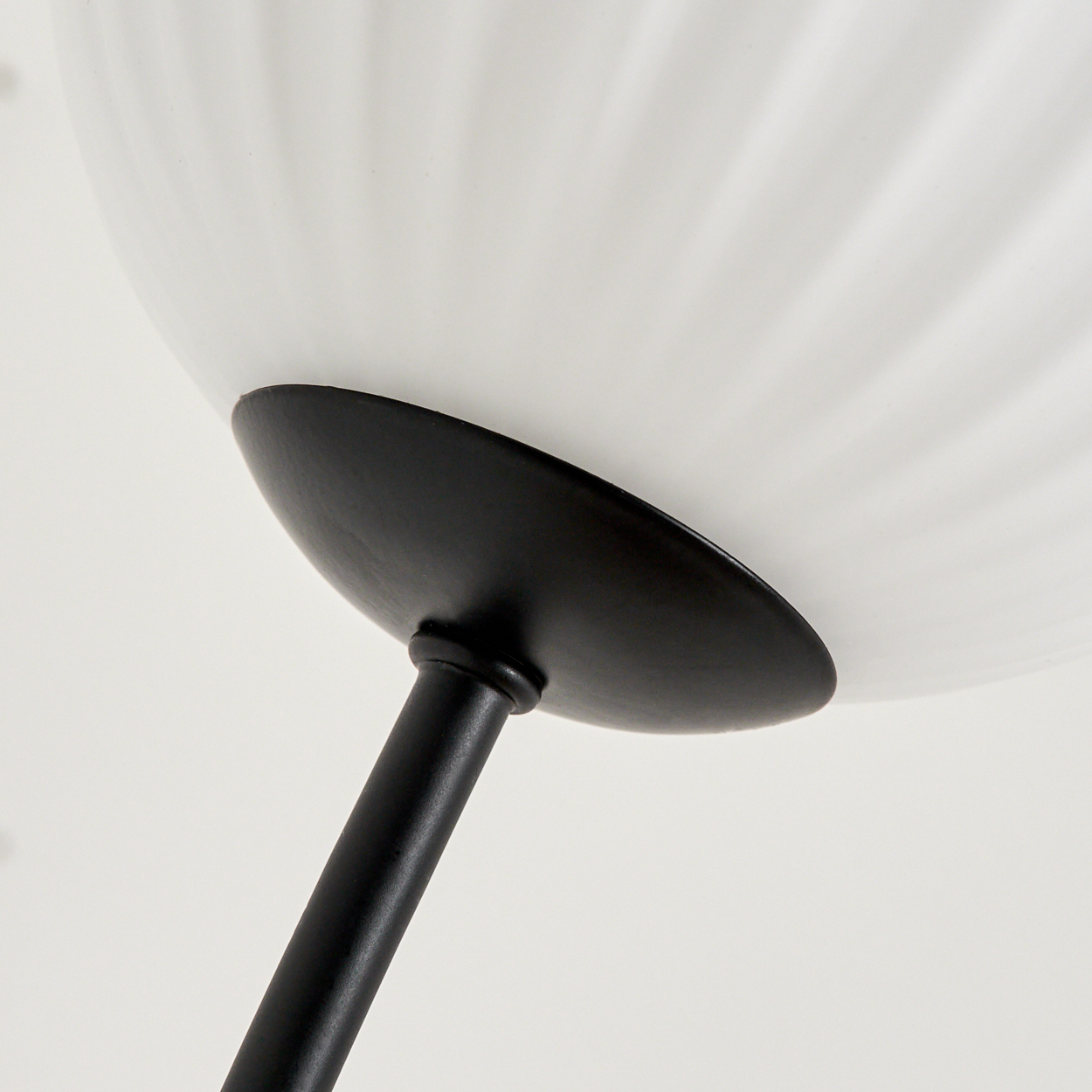 Nahaufnahme einer modernen Lampe. Sie hat einen weißen, geriffelten Lampenschirm über einem schwarzen, runden Sockel. Der Stiel der Lampe ist ebenfalls schwarz.