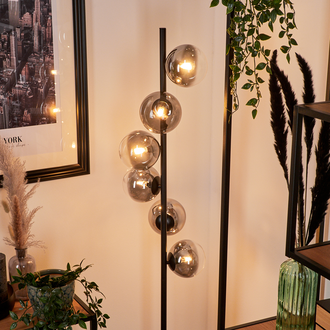 Eine moderne Stehlampe mit sechs Glaskugeln. Im Hintergrund sind ein gerahmtes New York-Bild und Pflanzen zu sehen.