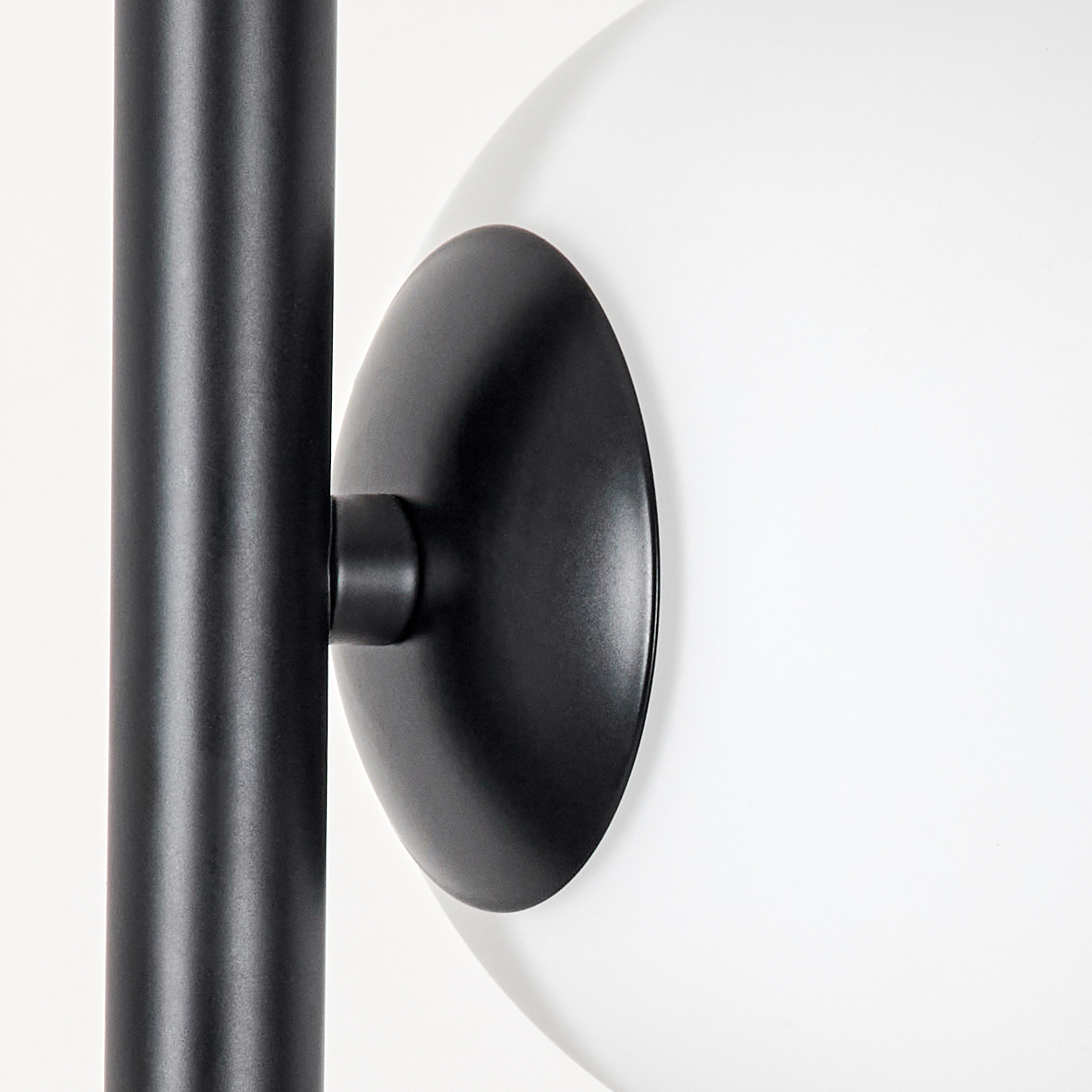 Nahaufnahme einer schwarzen Lampe. Eine schwarze Stange, eine schwarze kreisförmige Platte und ein weißes kugelförmiges Licht. Der Hintergrund ist weiß.