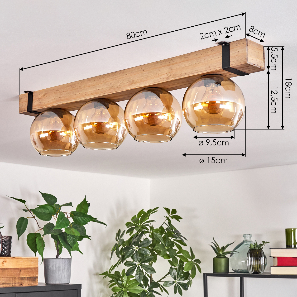 Deckenlampe mit vier bernsteinfarbenen Glaskugeln an einem Holzbalken. Pflanzen im Vordergrund, weißer Deckenhintergrund. Abmessungen gezeigt.