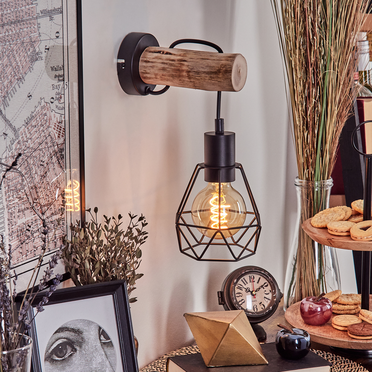Eine dekorative Szene mit einer Wandlampe, einer Karte, gerahmter Kunst, einer Uhr und Keksen. Die Lampe hat einen Holzbalken und eine umgitterte Glühbirne.