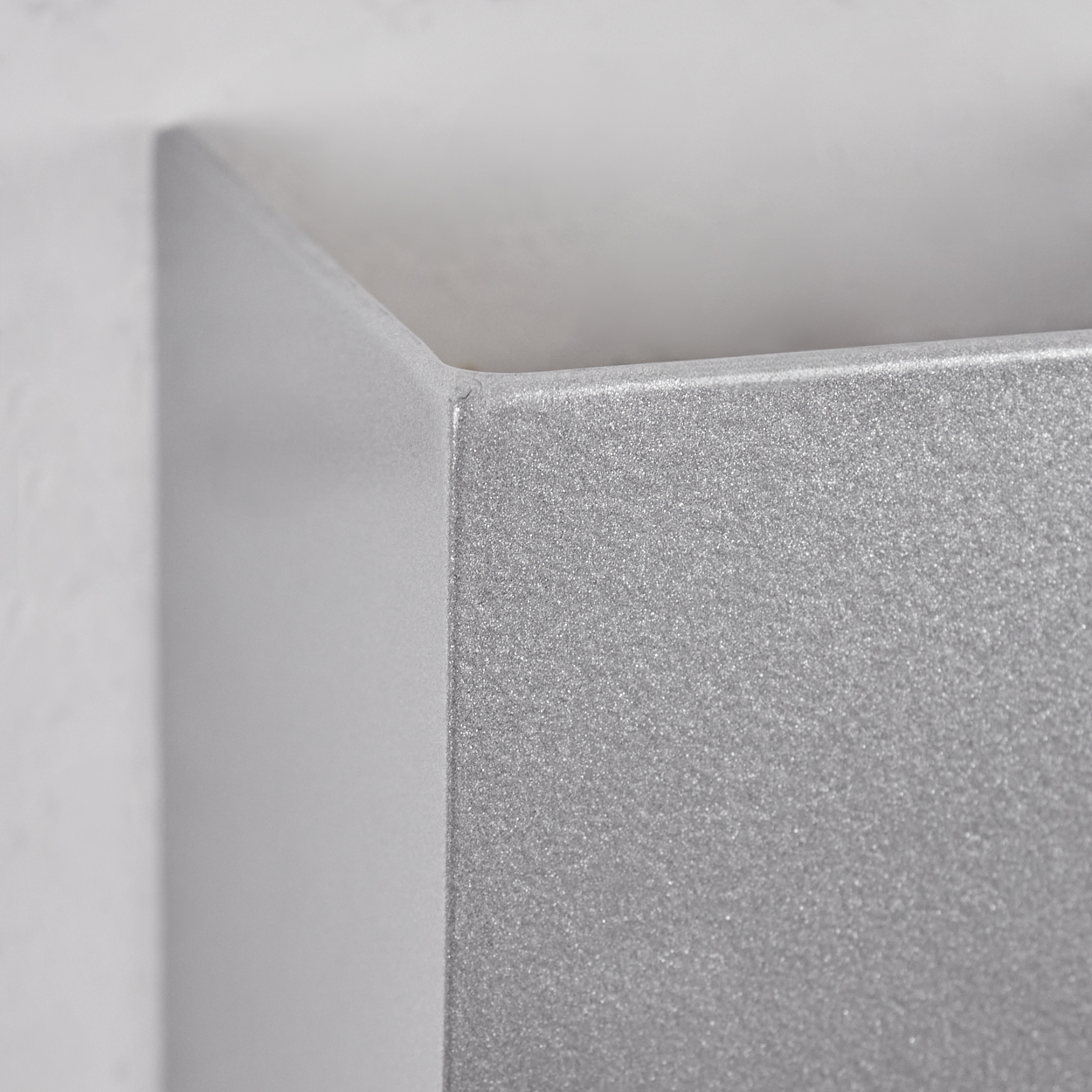 Nahaufnahme einer metallisch grauen Ecke. Die Oberfläche hat ein strukturiertes Aussehen. Der Hintergrund zeigt eine weiße Wand, die Ecke ist eckig.
