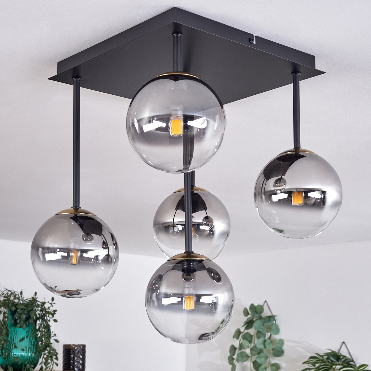 Moderne Deckenleuchte mit vier Glaskugeln, die von einer schwarzen quadratischen Basis hängen. Die Kugeln reflektieren den Raum.