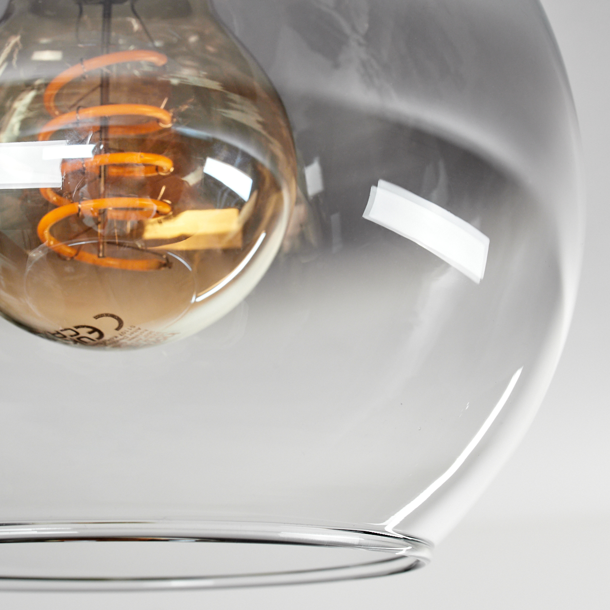 Nahaufnahme einer Glasleuchte. Im Inneren ist eine orangefarbene Glühbirne zu sehen. Das Glas hat einen rauchigen Grauton.