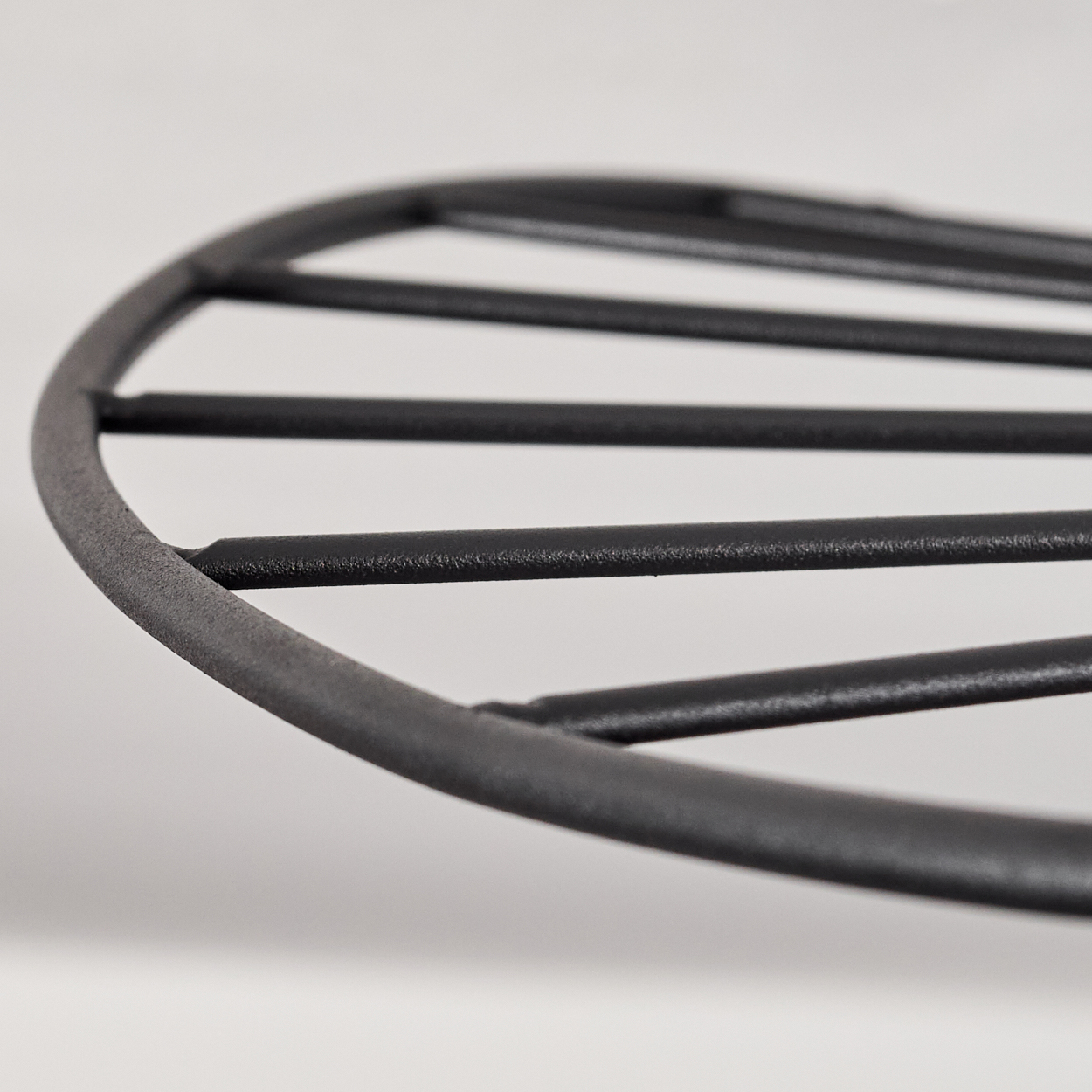 Nahaufnahme eines schwarzen Metallgrills. Der Grill ist kreisförmig mit mehreren parallelen Stäben. Ein weißer Hintergrund vervollständigt das Bild.