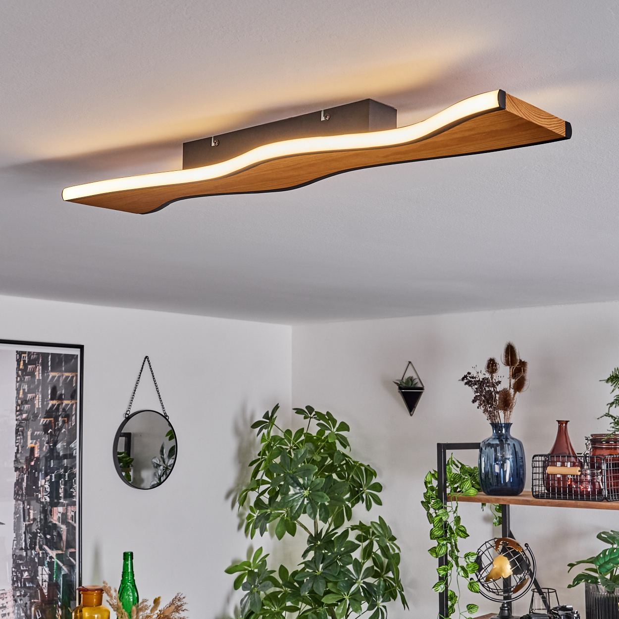 Eine Deckenleuchte aus Holz mit wellenförmigem Design ist installiert. Im Raum befinden sich Pflanzen, ein Spiegel und andere dekorative Gegenstände.