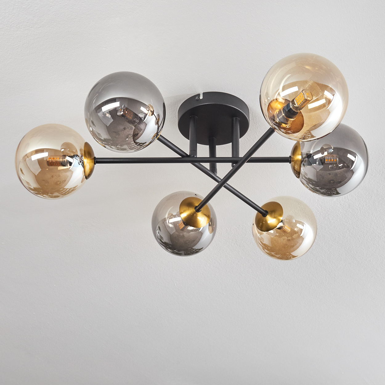 Eine Deckenleuchte mit sechs Glasglobus in Gold und Silber, schwarzen Armen und einem schwarzen Sockel an einer weißen Decke.