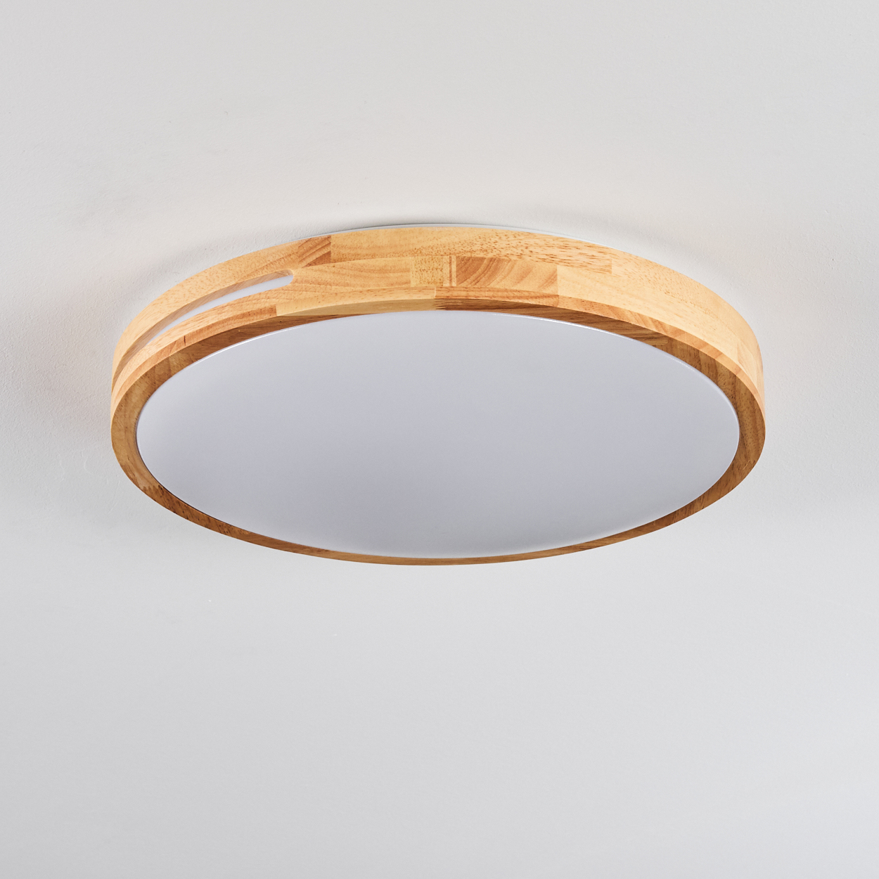 Eine runde Deckenleuchte aus Holz. Das Licht hat eine weiße, diffuse Mitte und einen hellen Holzmaserungsrahmen.