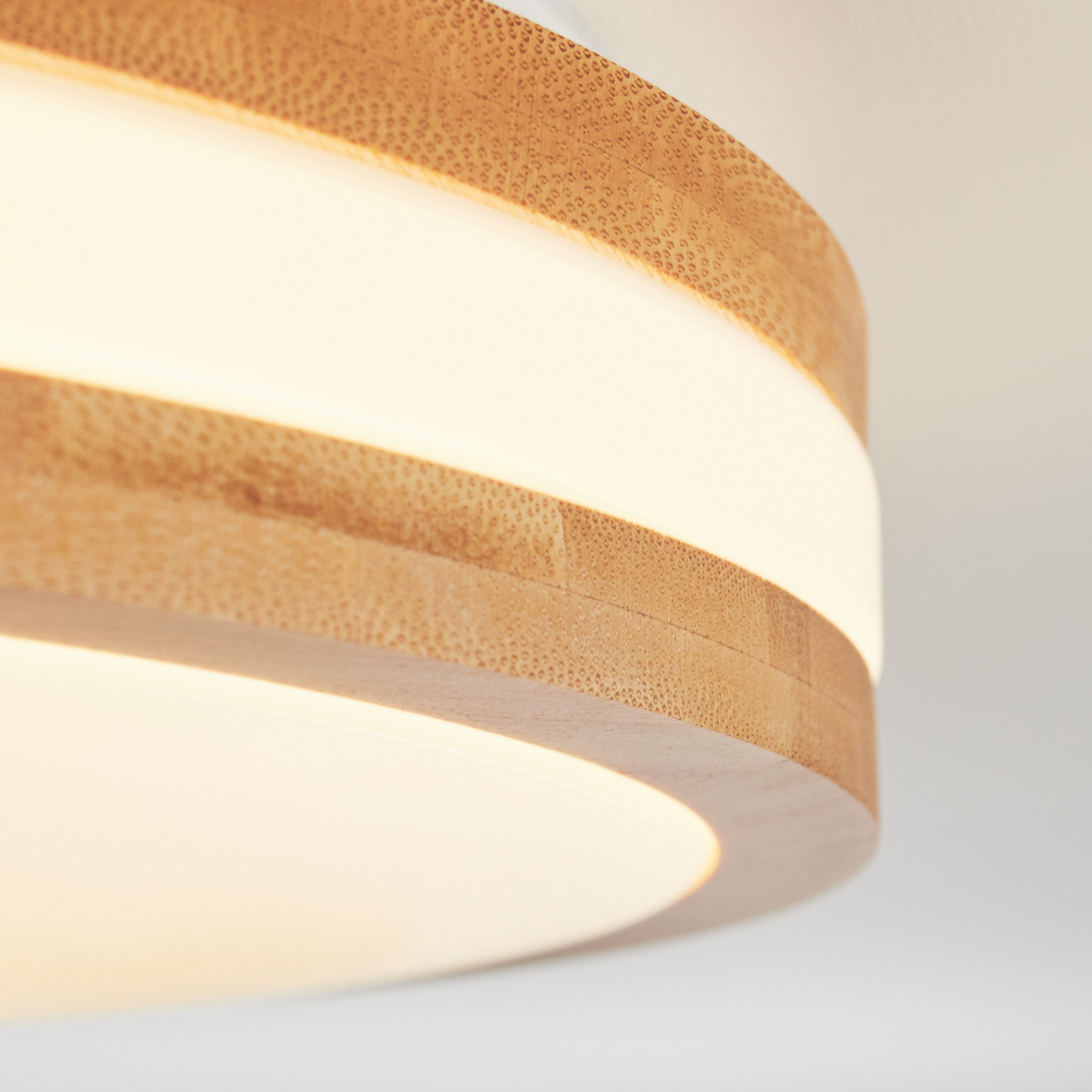 Nahaufnahme einer modernen Deckenleuchte mit Holzverkleidung und leuchtend weißem Licht. Das Licht ist kreisförmig.