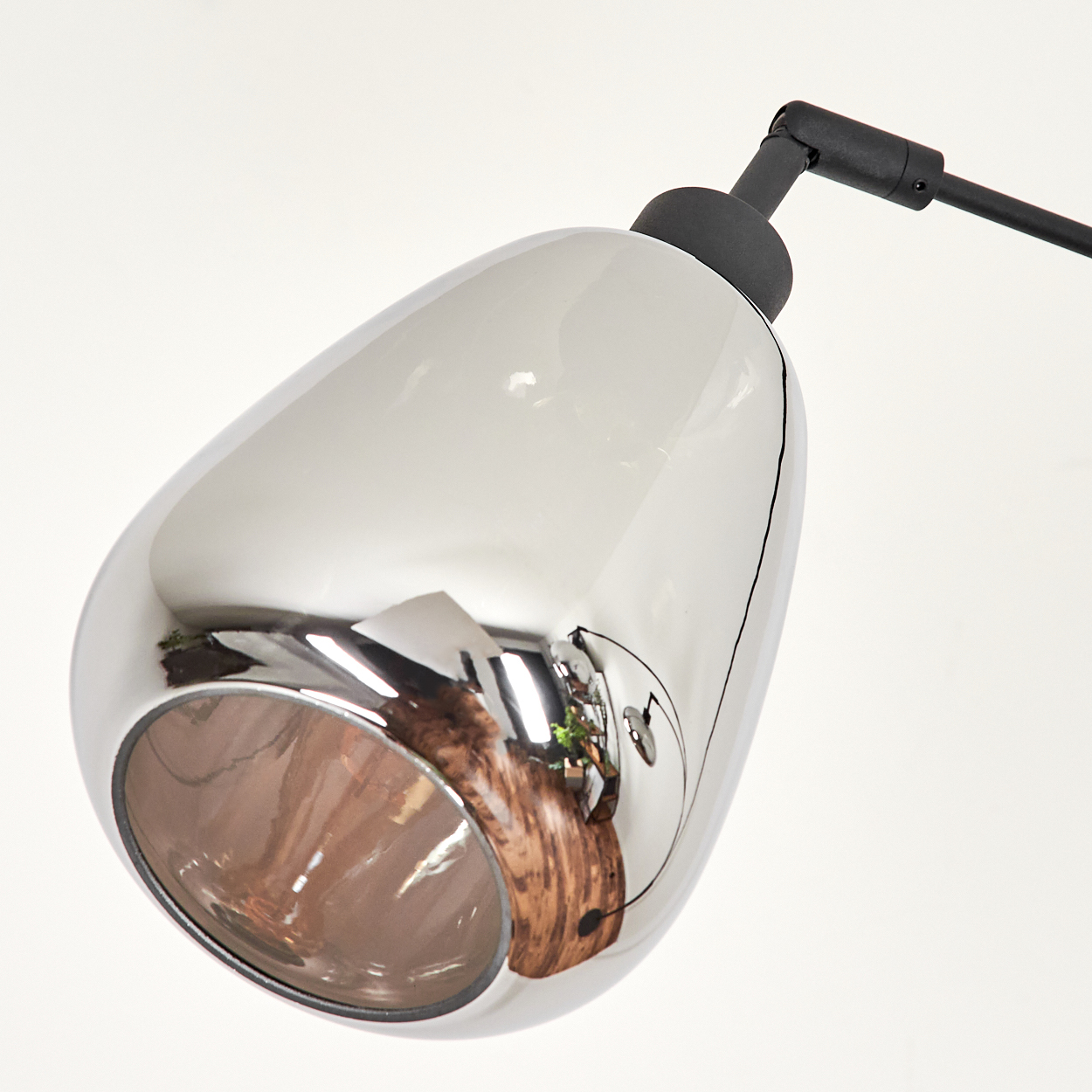 Eine Chromlampe mit tropfenförmigem Schirm und schwarzem Arm. Der Schirm spiegelt den Raum wider.
