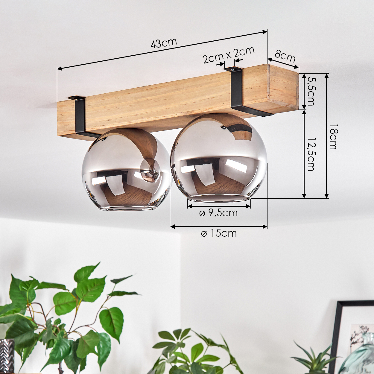 Ein Holzbalken mit zwei silbernen kugelförmigen Lichtern ist an der Decke montiert. Pflanzen sind im Vordergrund sichtbar.