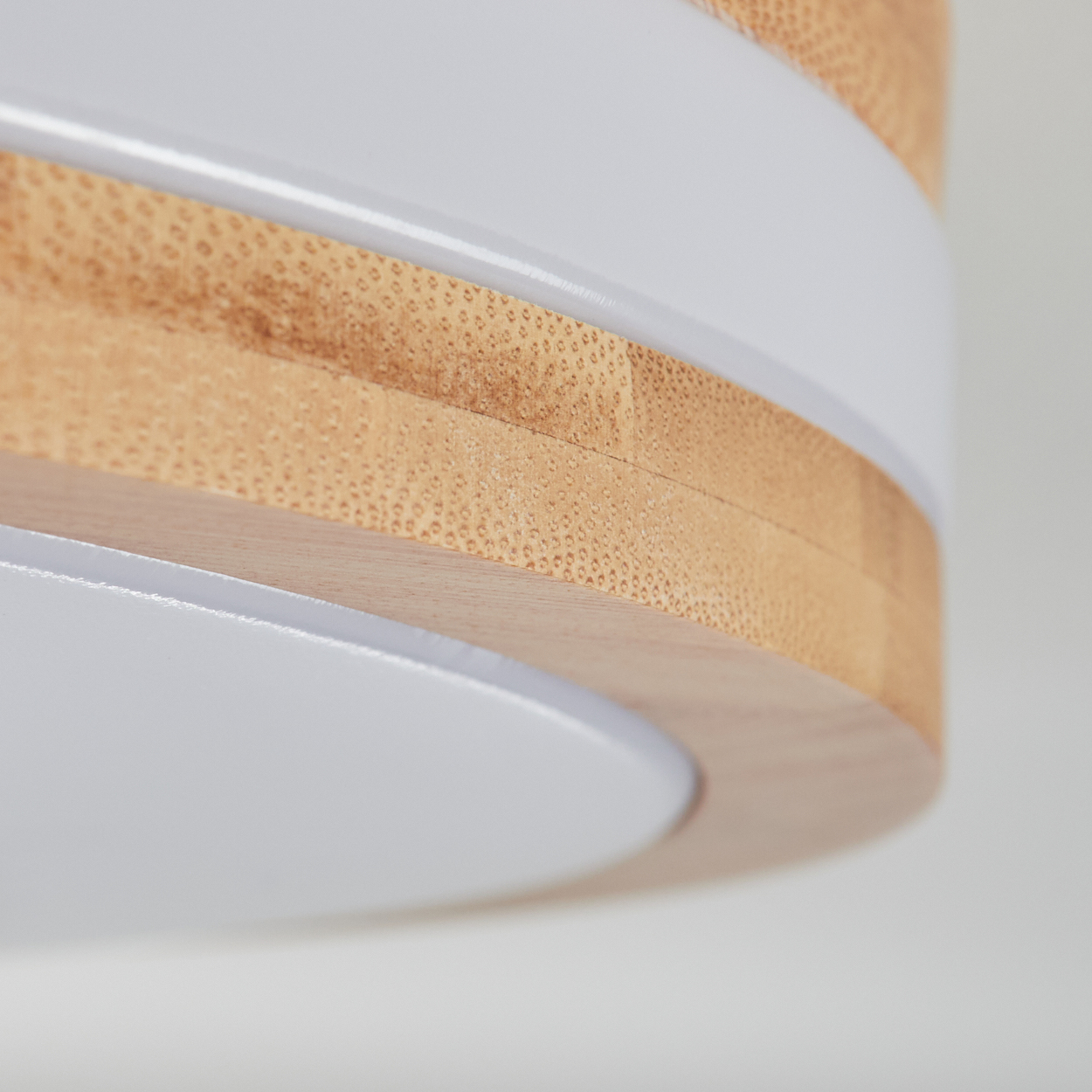 Nahaufnahme einer kreisförmigen Holzlampe mit weißen Akzenten. Die Lampe hat Schichten aus hellem Holz und weißen Bändern, vor weißem Hintergrund.