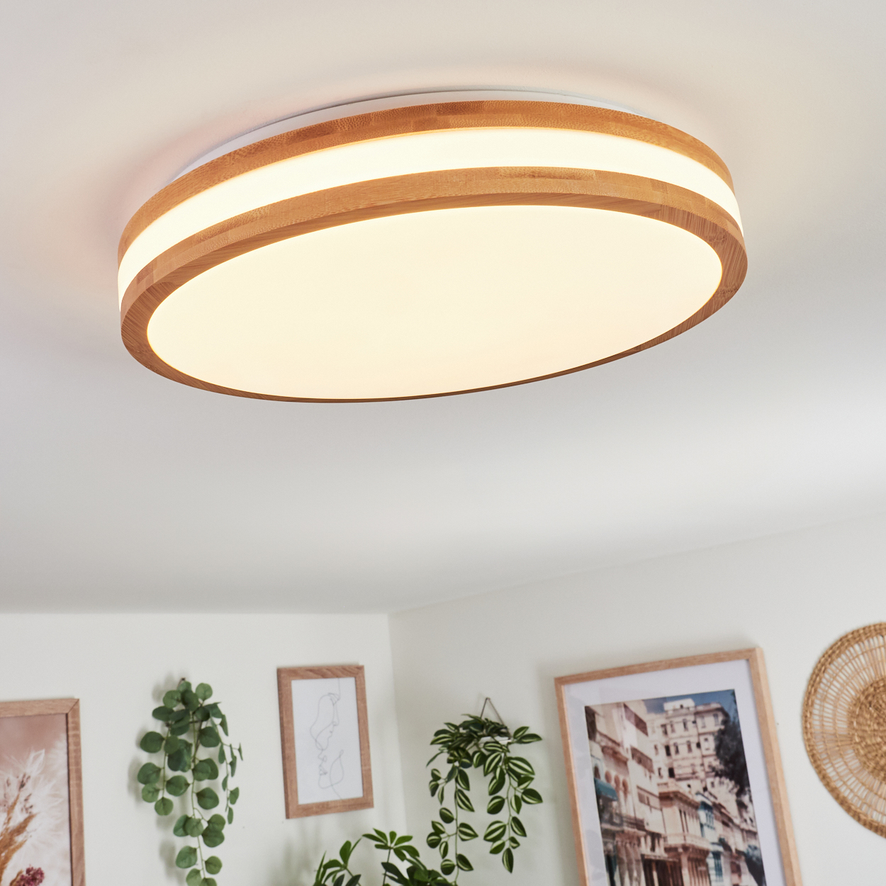 Eine moderne Deckenlampe mit Holzrahmen und weißem, ovalem Licht, das den Raum mit mehreren gerahmten Bildern und Pflanzen beleuchtet.