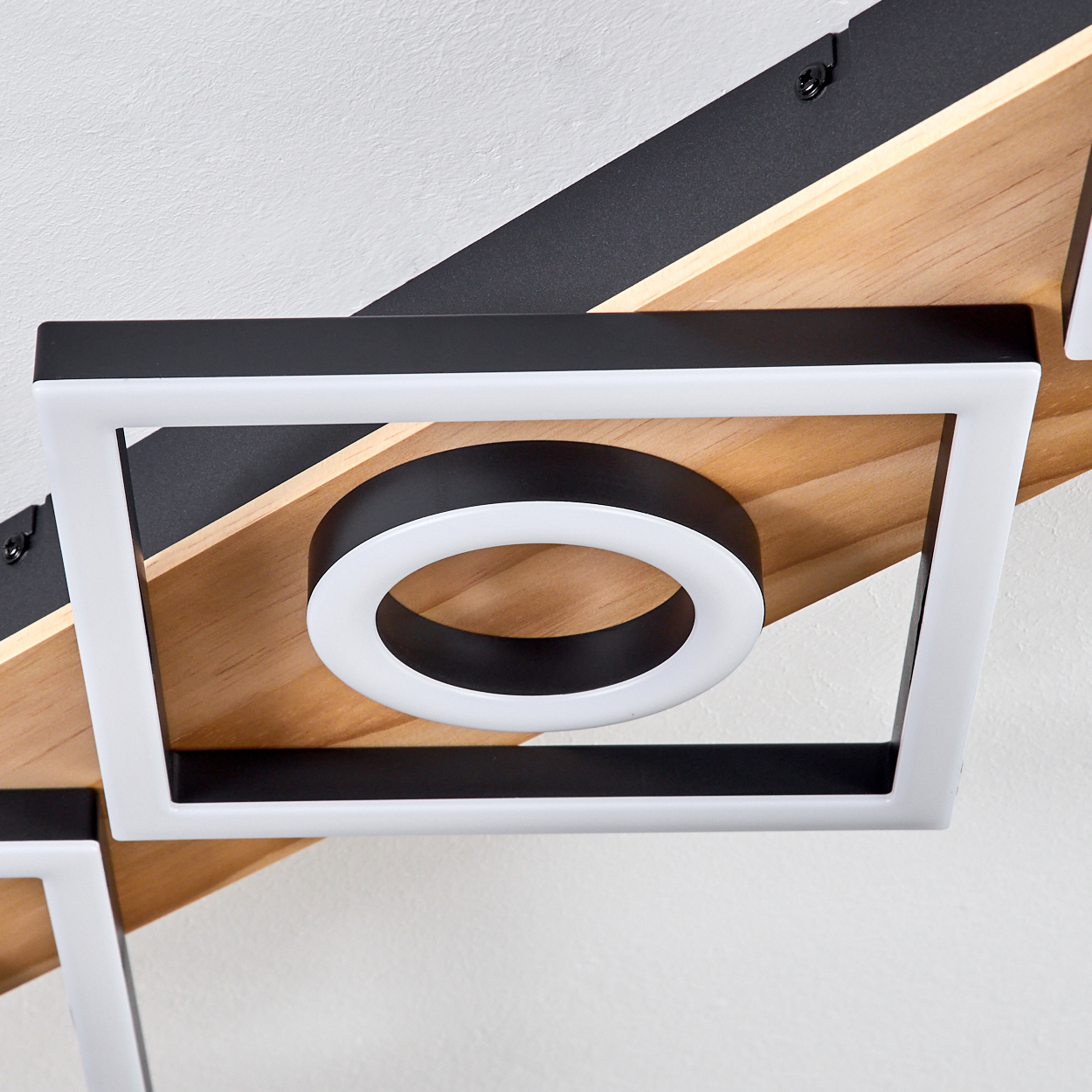 Eine moderne Deckenleuchte mit quadratischem Rahmen und kreisförmigem Licht. Der Hintergrund zeigt Holz- und Schwarzelemente.