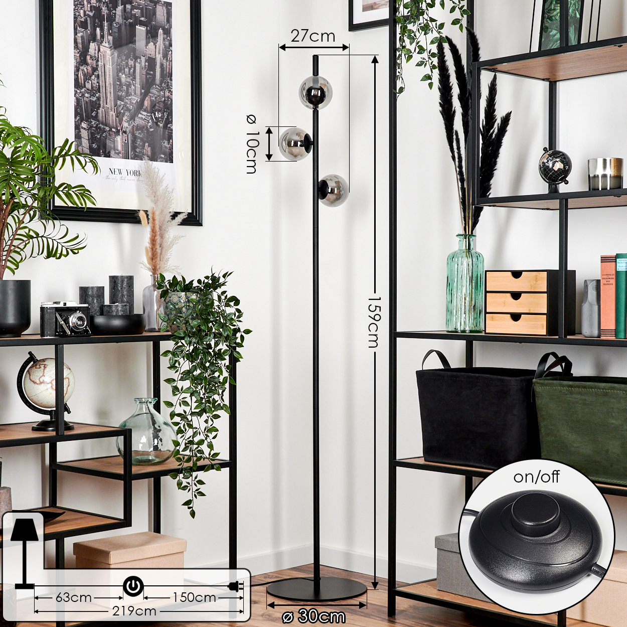 Eine schwarze Stehlampe mit drei kugelförmigen Lichtern neben einem Regal mit Dekorationen und einem New York City-Poster.