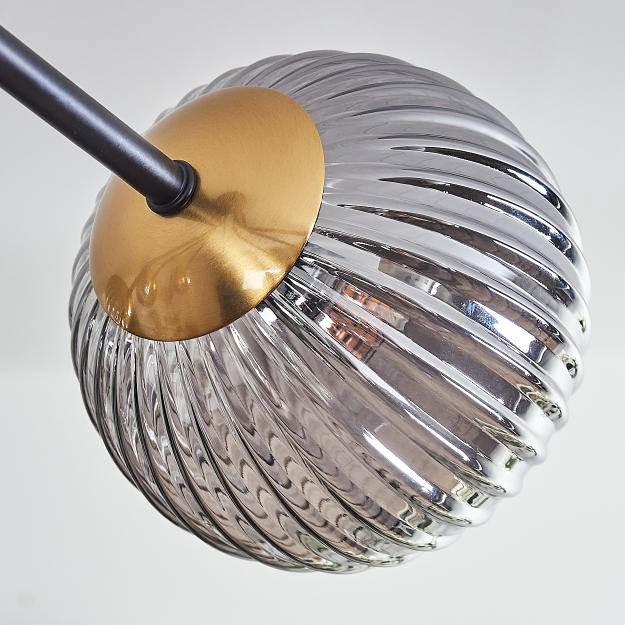 Eine moderne Leuchte. Sie hat einen kugelförmigen, gerippten Glasschirm mit goldfarbenem Sockel, der an einem schwarzen Metallarm befestigt ist.