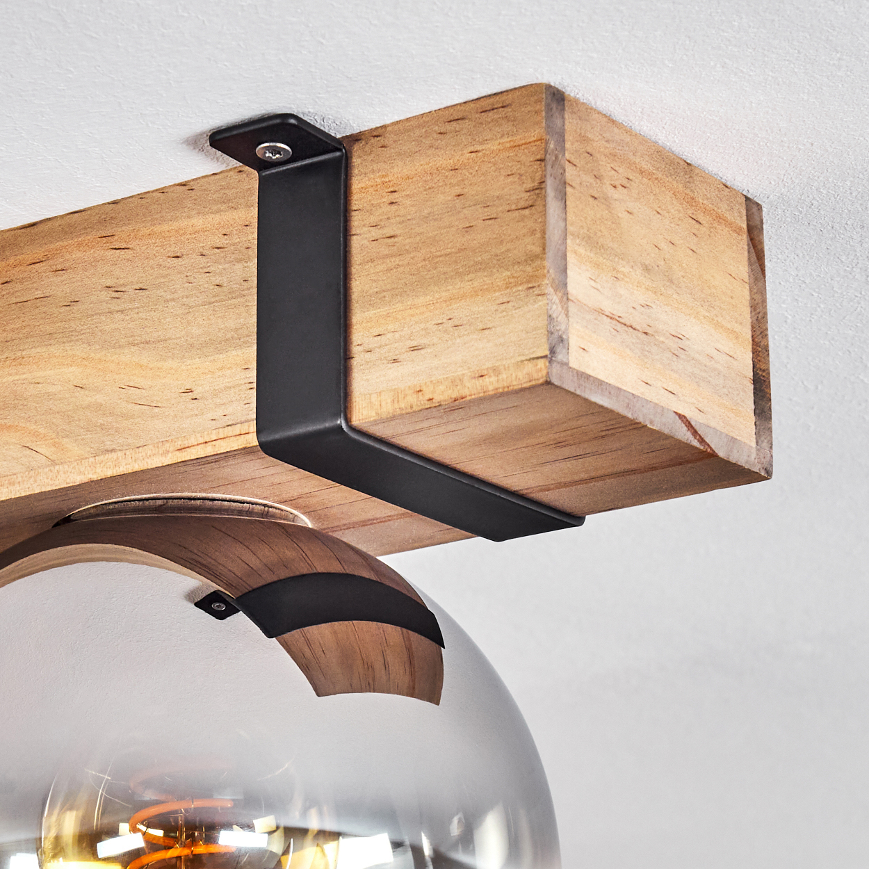 Holzbalken, von einer schwarzen Metallhalterung getragen, mit einer Glaskugelleuchte darunter. Der Hintergrund ist eine weiße Decke.