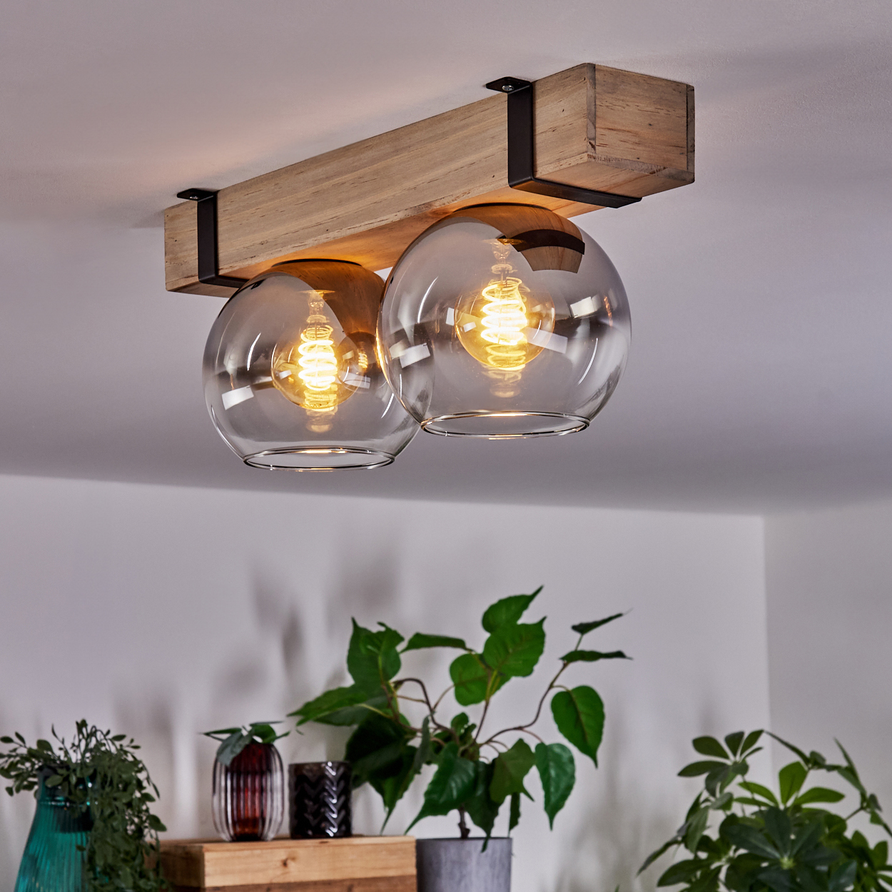 Eine Deckenleuchte mit zwei Glaskugelschirmen, die an einem Holzbalken befestigt sind. Pflanzen in Töpfen befinden sich im Vordergrund.
