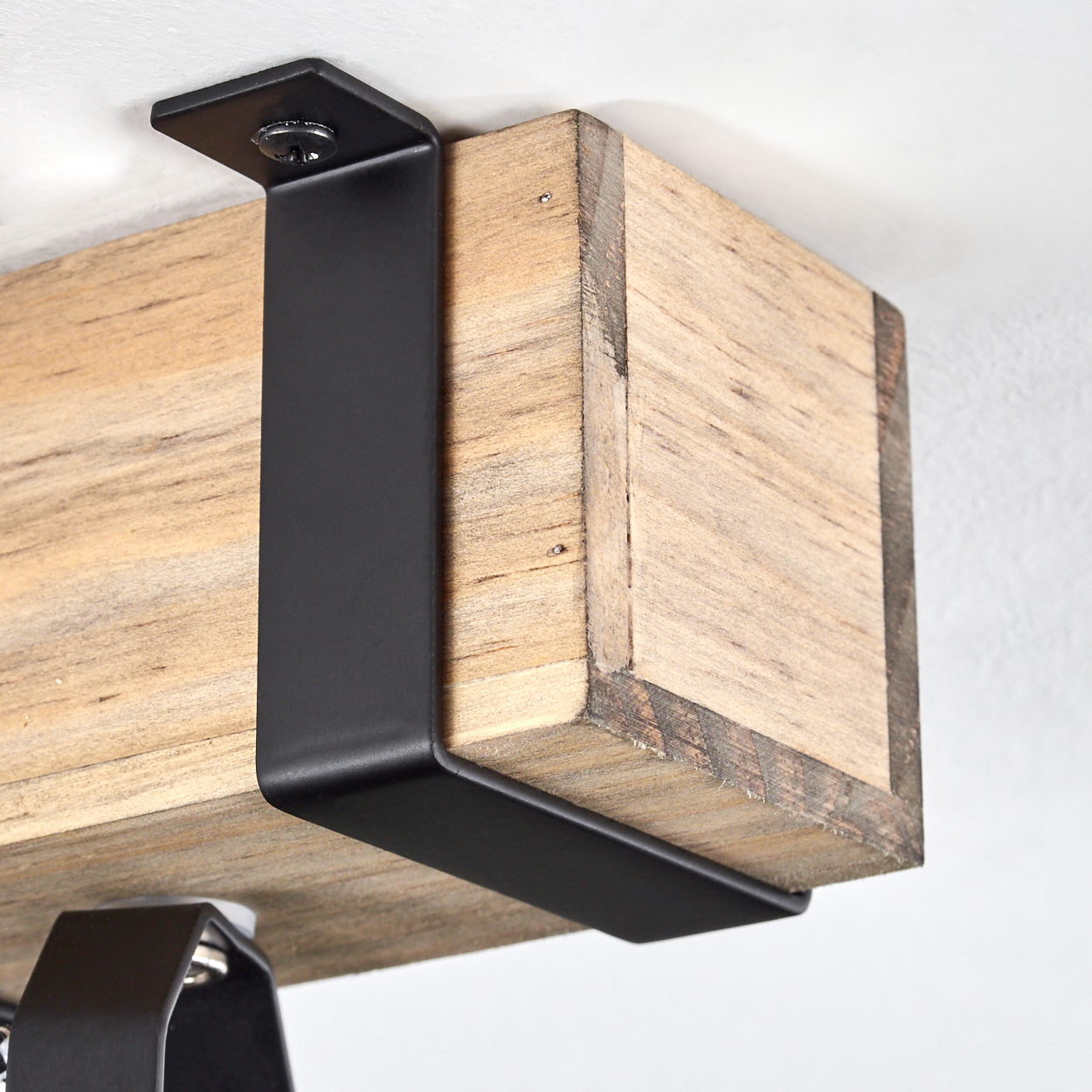 Ein Holzbalken, der von einer schwarzen Metallhalterung getragen wird. Die Halterung ist an der Decke befestigt.