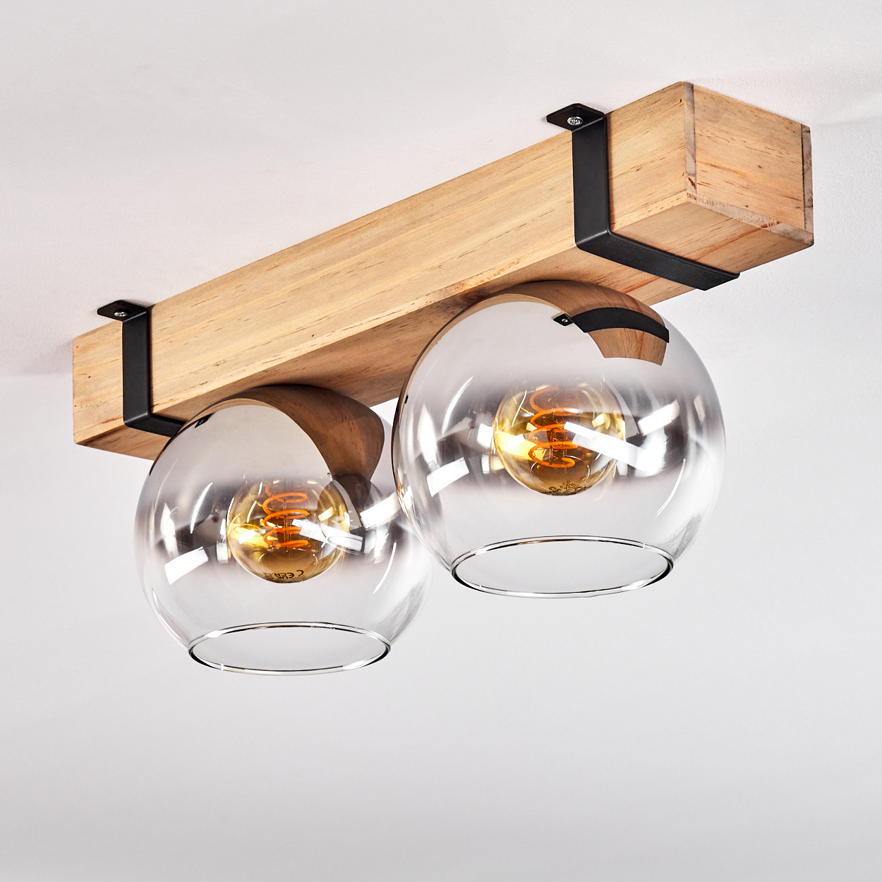 Eine Deckenleuchte mit zwei Glaskugelschirmen, Holzbalken, schwarzen Metallhalterungen und warmen Glühbirnen.