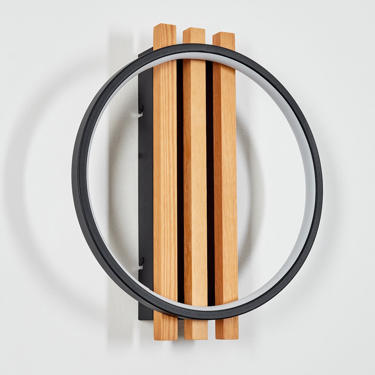 Eine moderne Wandleuchte mit schwarzem kreisförmigen Rahmen. Es hat Holzlatten und eine schwarze rechteckige Halterung an einer weißen Wand.