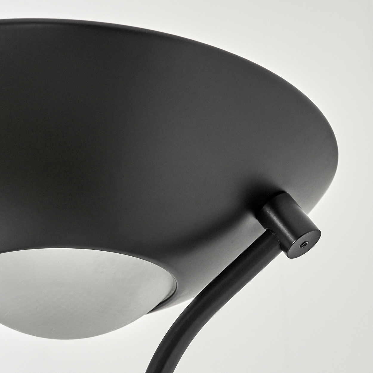 Nahaufnahme einer schwarzen Lampe. Die Lampe hat einen großen, flachen Schirm und einen gebogenen Arm. Der Hintergrund ist weiß.
