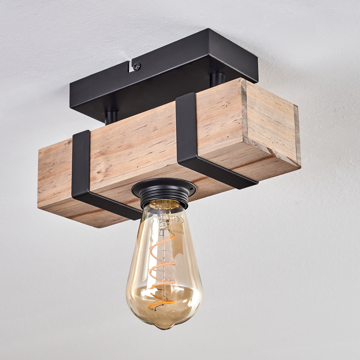Eine Deckenleuchte. Sie hat einen Holzbalken, schwarze Metallstützen und eine Edison-Glühbirne. Der Hintergrund ist eine weiße Decke.