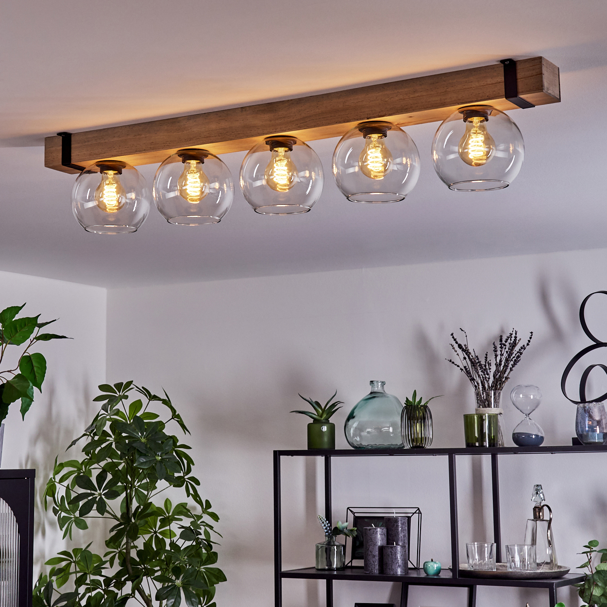 Eine Deckenleuchte mit fünf Glaskugelschirmen. Ein Holzbalken trägt die Lampen. Pflanzen und Dekorationen sind unten.