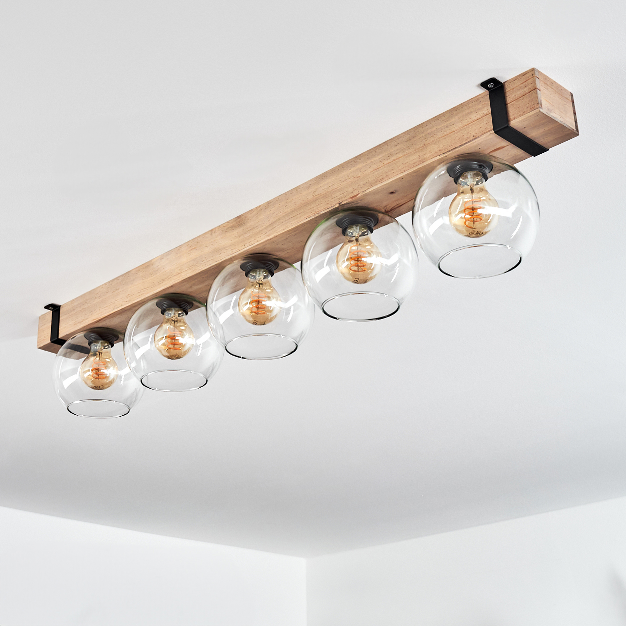 Eine Deckenleuchte aus Holzbalken mit fünf klaren Glaskugelschirmen, jeweils mit sichtbarer Edison-Glühbirne. Der Hintergrund ist eine weiße Decke.