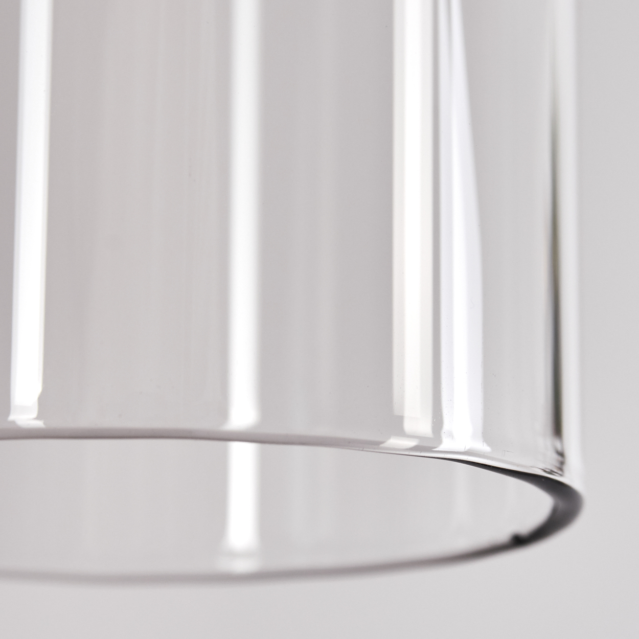 Nahaufnahme eines durchsichtigen Glaszylinders. Licht reflektiert sich im Glas. Der Hintergrund ist ein weiches, verschwommenes Weiß.