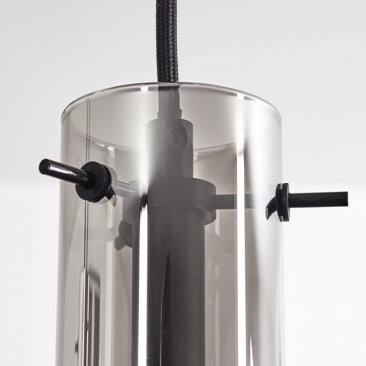 Nahaufnahme einer modernen Lampe. Sie hat einen zylindrischen, rauchigen Glasschirm, schwarze Metallakzente und ein schwarzes, stoffbezogenes Kabel.