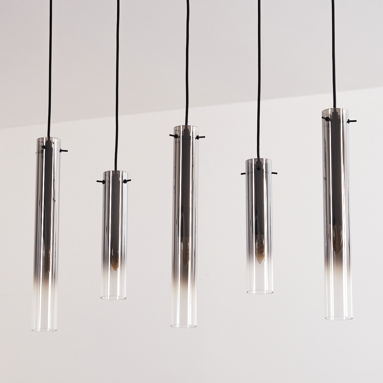 Fünf zylindrische Pendelleuchten hängen von der Decke. Jede hat eine Glastube mit Farbverlauf und ein schwarzes Kabel.
