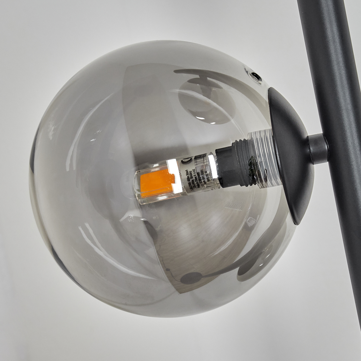 Nahaufnahme einer grauen Glaskugel mit eingebautem orangenen Licht, befestigt an einem schwarzen Metallrahmen, vor weißem Hintergrund.