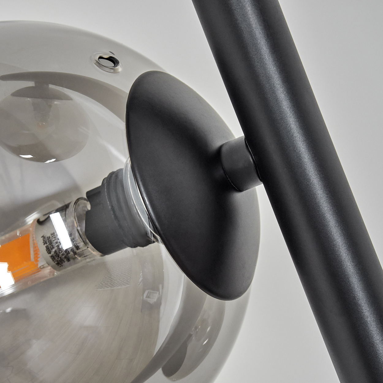 Nahaufnahme einer modernen Lampe. Eine klare Glaskugel mit einem schwarzen Metallarm und einer schwarzen Scheibe. Die Glühbirne hat einen orangefarbenen Schein.
