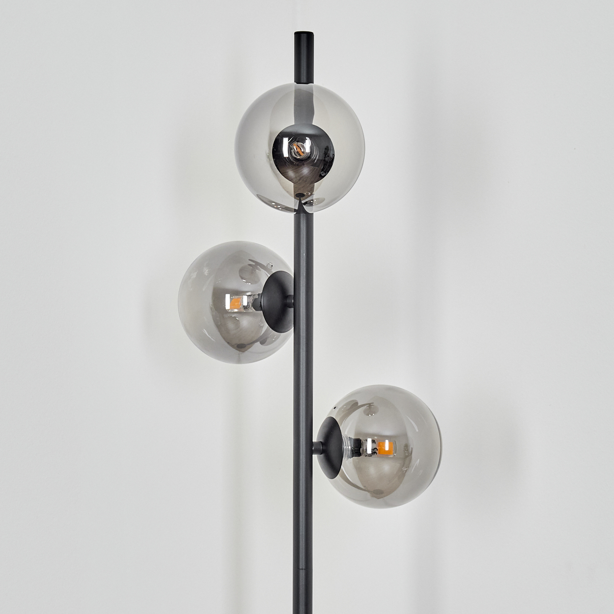 Eine moderne Lampe mit drei rauchfarbenen Glaskugelschirmen. Die Lampe ist schwarz mit einer weißen Wand im Hintergrund.