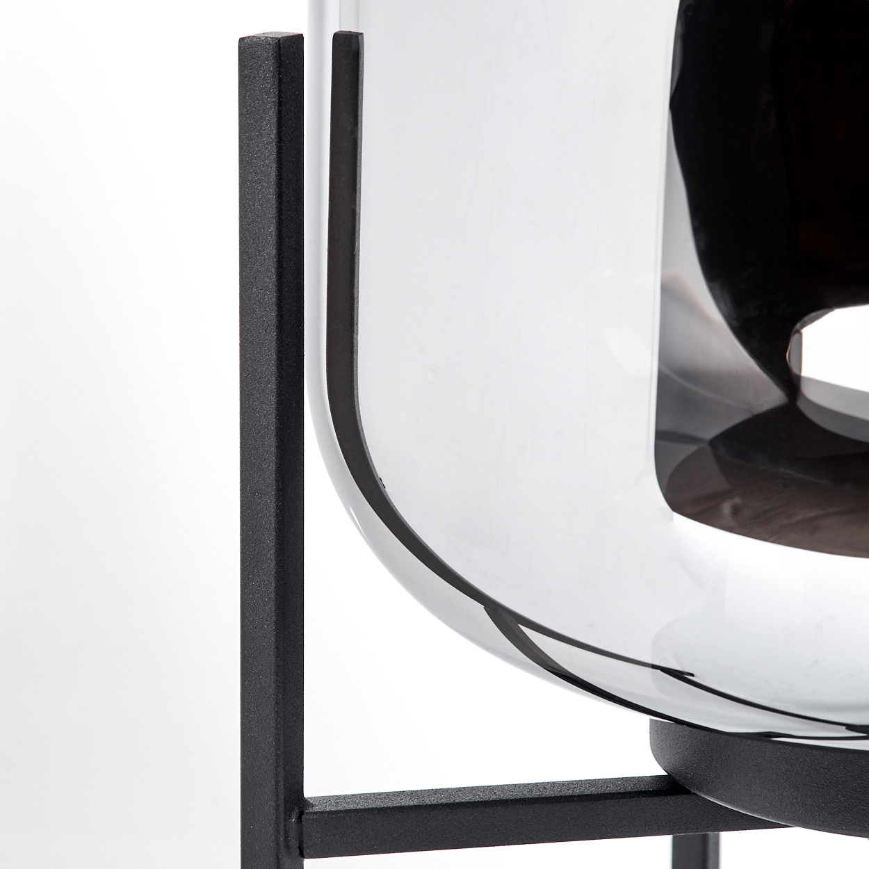 Eine klare Glasschale auf einem schwarzen Metallständer. Das Glas reflektiert die Umgebung. Der Ständer hat vertikale und horizontale Stützen.