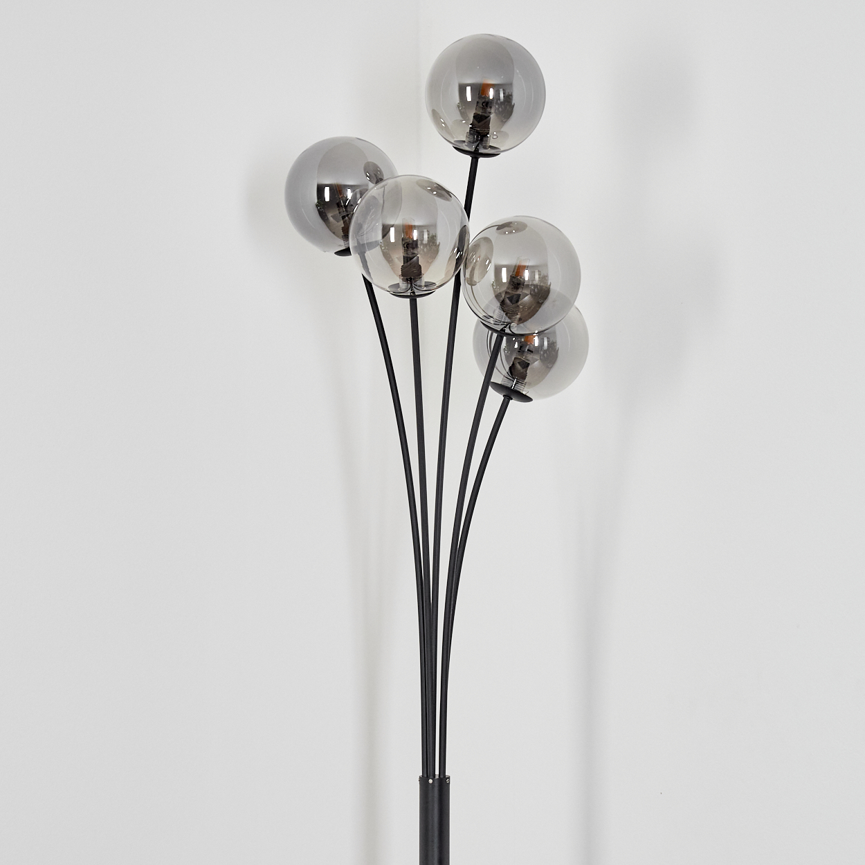 Eine moderne Stehlampe mit sechs kugelförmigen, verspiegelten Glasschirmen. Die schwarzen Stiele erheben sich von einem schwarzen Sockel vor einer weißen Wand.