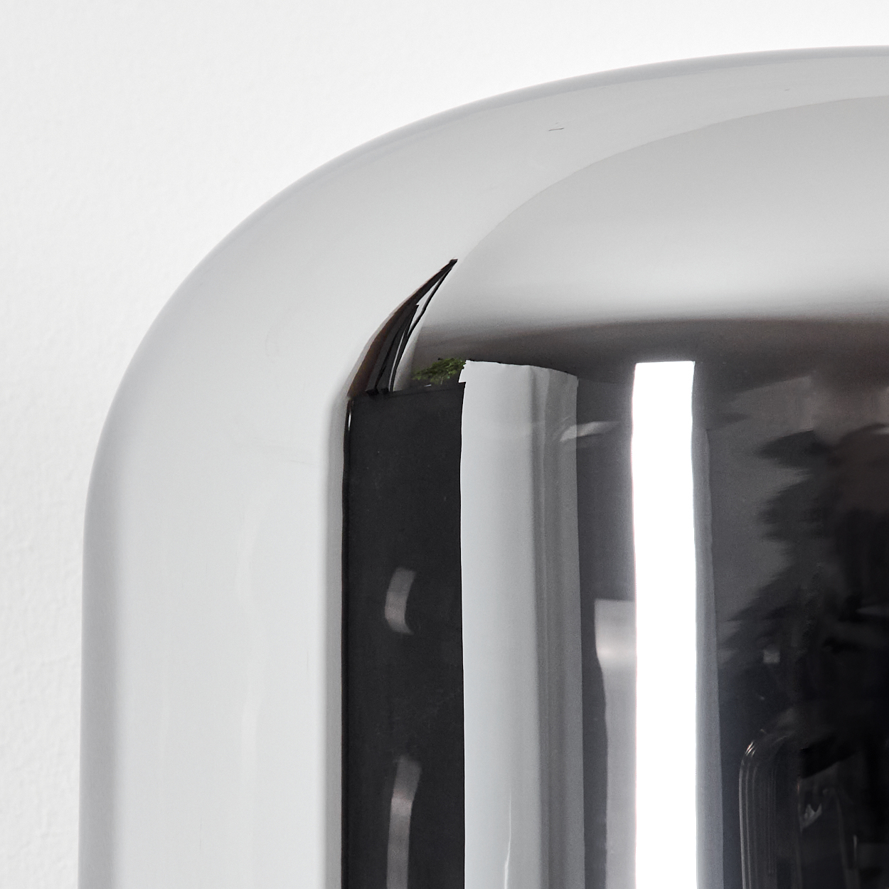 Nahaufnahme einer gewölbten, reflektierenden Oberfläche, möglicherweise Metall oder Glas, mit dunklem, rechteckigem Element und weißer Wand.