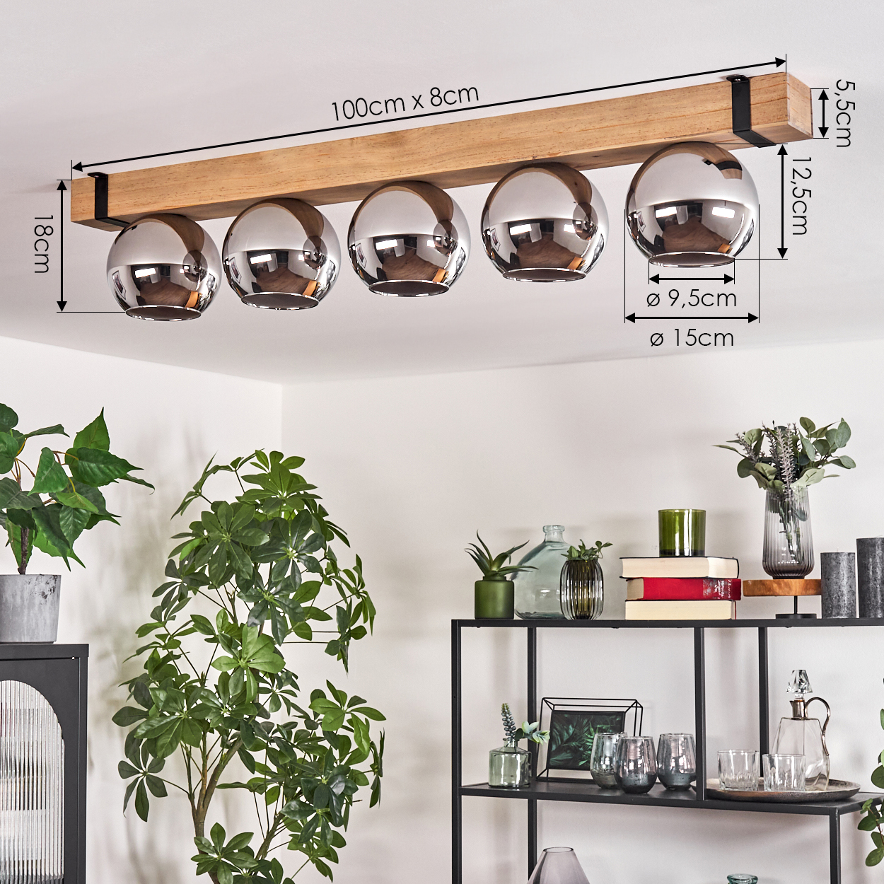 Ein Holzbalken mit fünf glänzenden, kugelförmigen Lichtern hängt von der Decke. Pflanzen und ein Regal mit Dekorationen befinden sich im Vordergrund.