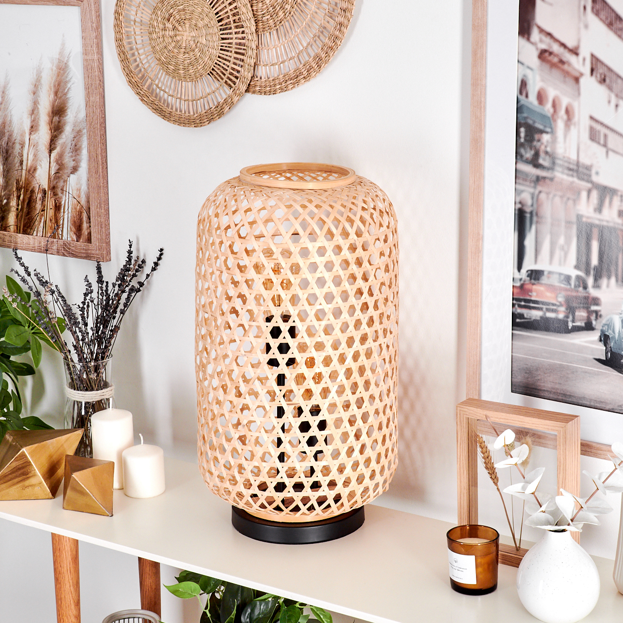 Eine dekorative Innenszene mit einer gewebten Lampe, Kerzen, Kunst und Pflanzen auf einem weißen Konsolentisch.