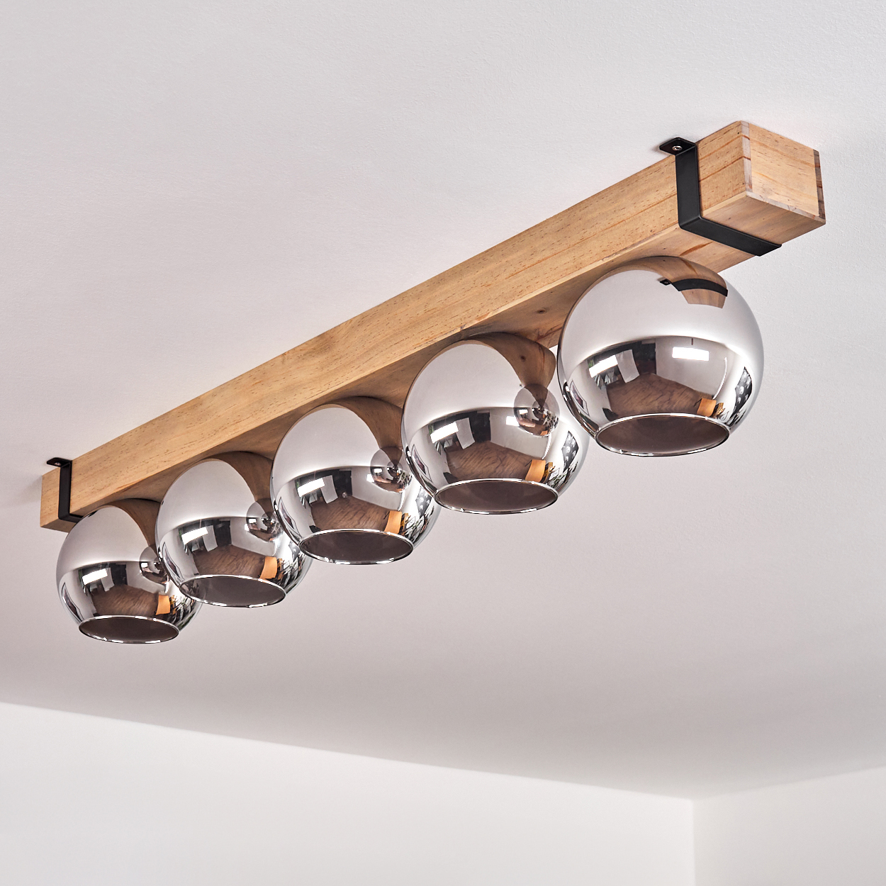 Eine Deckenleuchte mit fünf Chromkugel-Lampen, die an einem Holzbalken befestigt sind und an einer weißen Decke montiert sind.